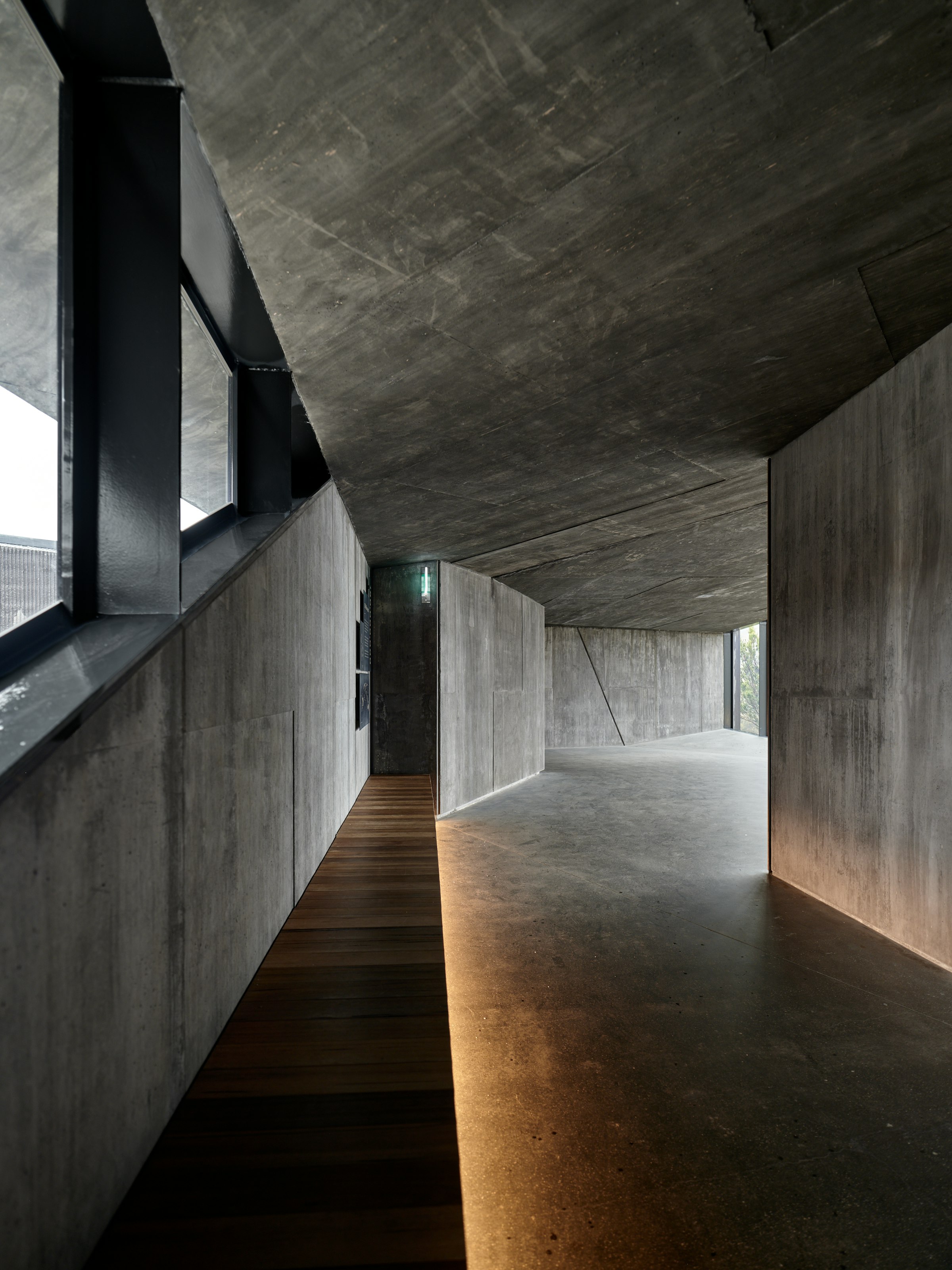 A long concrete interior with a warm timber walkway and soft recessed lighting